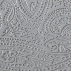 May include: A close-up of a white embossed design with a paisley pattern. The design is made up of small dots, swirls, and lines.