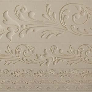 May include: A white silicone mold with three different decorative patterns. The mold features intricate designs of swirls and leaves.