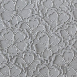 Puede incluir: Primer plano de un molde de silicona texturizado gris con un patrón repetitivo de flores en relieve. El molde está diseñado para hornear y decorar pasteles y otros postres.
