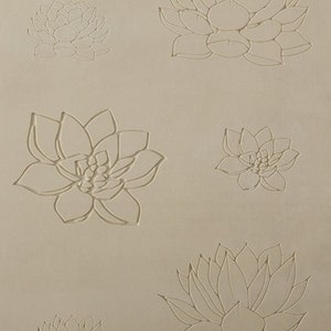 Könnte beinhalten: Eine weiße Fondantplatte mit fünf geprägten Lotusblüten-Designs. Die Blüten sind mit einer dünnen Linie umrandet und haben ein zartes, filigranes Design.