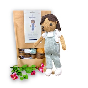 May include: Knitting kit for a doll named Girl June. The kit includes yarn in shades of brown, white, and green, and a pattern for a doll with brown hair and a white shirt and blue overalls.