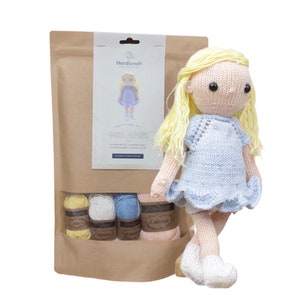 May include: Knitting kit for a doll with a blue dress and blonde hair. The kit includes yarn in yellow, white, light blue, and pink. The kit is packaged in a brown paper bag with a label that says "Hardicraft" and "Girl April".