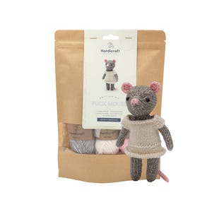 May include: A knitting kit for a Puck Mouse, featuring a brown paper pouch with a label showing the finished toy, and a completed grey knitted mouse doll with pink ears and nose, wearing a beige dress, standing in front of the packaging.
