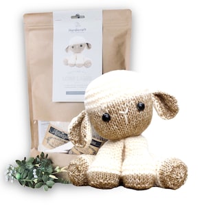 May include: Knitting kit to make a brown and white knitted lamb. The kit includes yarn, needles, and instructions. The finished lamb is sitting on a white background.