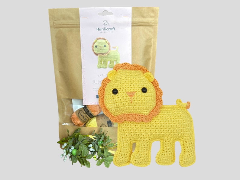 May include: A yellow crochet lion with an orange mane and tail, next to a craft kit bag. The kit includes yarn and a printed label with a lion illustration and the text "Hardicraft". The lion is approximately 6 inches tall.