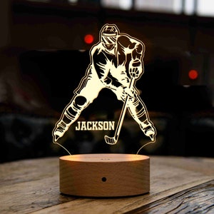 May include: A wooden base with a 3D printed hockey player silhouette. The player is in a skating position with a stick and puck. The name "JACKSON" is printed on the base.