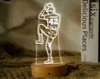 May include: A white 3D printed night light shaped like a baseball player in a pitching pose. The player is wearing a jersey with the name "RICHARD" and the number "42" on the back. The night light is on a wooden base.