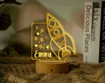 May include: A yellow rocket ship with stars and the name "Emma" on a wooden base. The rocket ship is a night light.