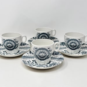 May include: A set of three white ceramic cups and matching saucers, each decorated with a dark blue floral mandala pattern. The cups feature a rounded handle and a ribbed texture, while the saucers display a coordinating intricate botanical border.