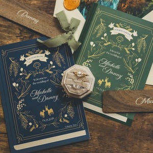 May include: A wedding invitation suite with a blue and green theme, including a wooden name tag and a ring box. The invitation features the names "Michelle and Danny" and the date 04.29.2036.