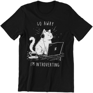 Könnte beinhalten: Schwarzes T-Shirt mit einer weißen Illustration einer Katze, die Kopfhörer trägt und einen Laptop benutzt. Der Text "Go Away I'm Introverting" ist unter der Katze aufgedruckt.