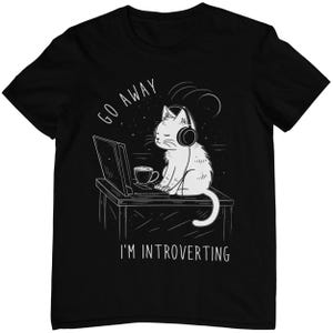 Könnte beinhalten: Schwarzes T-Shirt mit einer weißen Illustration einer Katze, die Kopfhörer trägt und an einem Laptop mit einer Tasse Kaffee sitzt. Der Text "Go Away I'm Introverting" ist unter der Katze aufgedruckt.