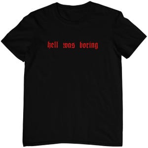 Könnte beinhalten: Schwarzes T-Shirt mit dem Text "hell was boring" in roter gotischer Schrift.