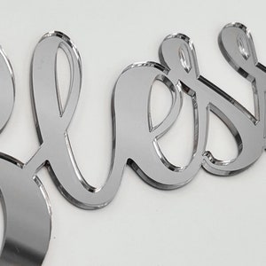 May include: Silver mirror acrylic word "Bless" in a cursive font.