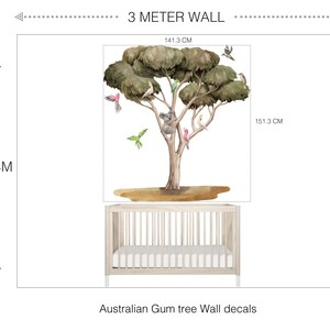 Op de afbeelding: Een 3 meter hoge wanddecoratie met een grote eucalyptusboom met een koala, vogels en een buideldier. De decoratie is afgebeeld op een witte muur met een wieg ervoor. De decoratie is 141,3 cm breed en 151,3 cm hoog. Australische Eucalyptusboom wanddecoratie.
