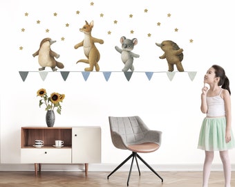 May include: A white wall with a blue and gray bunting with four Australian animals walking on it. The animals are a koala, a kangaroo, an echidna, and a platypus. There are gold stars scattered around the bunting. A young girl is standing to the right of the wall, looking up at the animals.