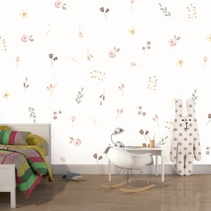 May include: A white wall with a floral pattern in shades of pink, yellow, and brown. A white bed with a colourful patchwork quilt is in the foreground. A white rocking chair and a brown polka dot bunny are also in the room.