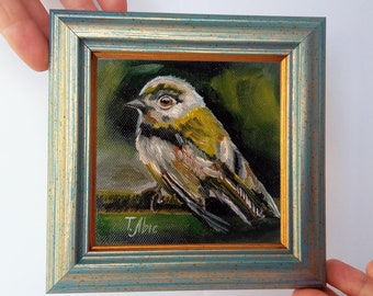May include: A framed oil painting of a small bird with yellow and green feathers. The bird is perched on a branch and is looking to the left. The painting is signed "T. Abic" in the lower right corner.