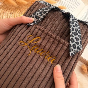 Peut inclure: Une housse de bouillotte en velours c&ocirc;tel&eacute; marron avec une surface textur&eacute;e &agrave; c&ocirc;tes et un lien en tissu &agrave; motif l&eacute;opard sur le dessus. Le pr&eacute;nom "Laura" est brod&eacute; en fil dor&eacute; cursif sur le devant de la housse, qui comporte une petite poche.