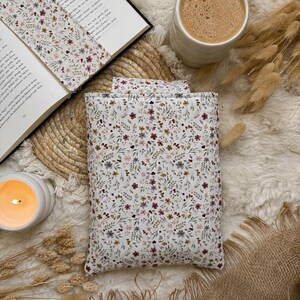 Eine rechteckige Buchbeutel aus Stoff mit weißem Hintergrund und einem zarten Blumenmuster in gedeckten Rot-, Braun- und Grüntönen. Die Hülle besteht aus gestepptem Textil und zeigt durchgehend einen einheitlichen botanischen Aufdruck.