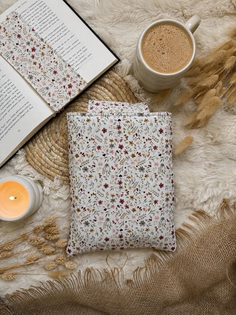 Eine rechteckige Buchbeutel aus Stoff mit weißem Hintergrund und einem zarten Blumenmuster in gedeckten Rot-, Braun- und Grüntönen. Die Hülle besteht aus gestepptem Textil und zeigt durchgehend einen einheitlichen botanischen Aufdruck.