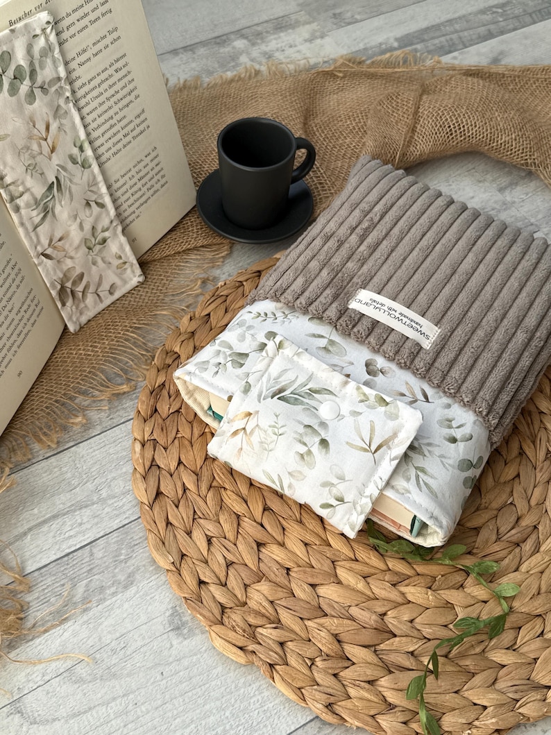 Gepolsterte Buchhülle für Taschenbücher, mit floralem Muster und Label „SweetWoollyLand“, schützt Bücher unterwegs.