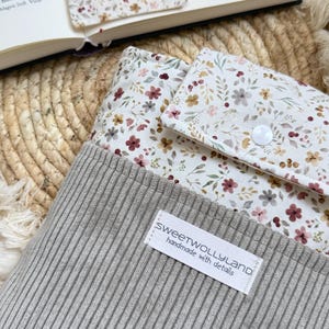 Eine graue, gerippte Buchhülle mit einem weißen Blumenmuster aus kleinen roten, rosafarbenen und braunen Blüten Stoff Buchhülle schützt Bücher vor Knicken und Kratzern und eignet sich für Reisen, Schule, Uni oder den Alltag.