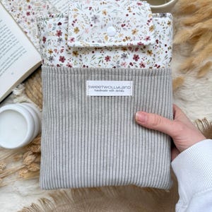 Personalisierte Buchhülle mit hochwertiger Namensstickerei auf grauem Cord und floralem Stoff als individuelles Geschenk.