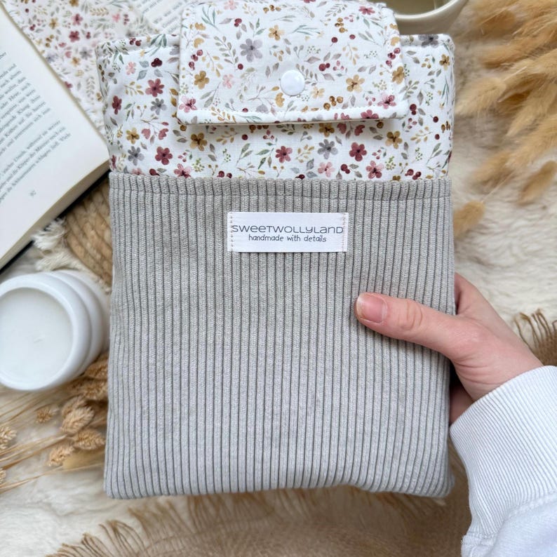 Personalisierte Buchhülle mit hochwertiger Namensstickerei auf grauem Cord und floralem Stoff als individuelles Geschenk.