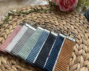 Peut inclure: Un ensemble de huit porte-clés avec des lanières en tissu de différentes couleurs et des anneaux de clés argentés. Les lanières sont en velours côtelé, en lin et en coton.