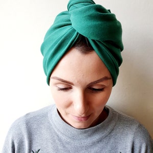 May include: A green turban style hair wrap made of soft fabric. The wrap is tied in a knot on top of the head.