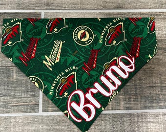 May include: Green and white dog bandana with a repeated pattern of the Minnesota Wild hockey team logo. The bandana has the name "Bruno" written in white on the bottom right corner.