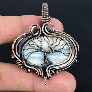 May include: Copper wire wrapped pendant featuring a tree of life design with a blue and white agate stone.