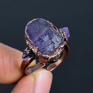 May include: A copper ring with a large, raw amethyst stone set in the center. Two smaller amethyst stones are set on either side of the main stone.