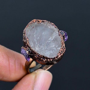 Puede incluir: Un anillo de cobre con una piedra de cuarzo transparente y dos pequeñas piedras de amatista a los lados.