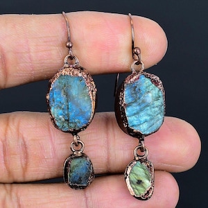 Könnte beinhalten: Kupferne Ohrringe mit zwei Labradorit-Steinen. Der größere Stein ist hellblau mit irisierenden grün- und blautönen. Der kleinere Stein ist dunkelgrün mit irisierenden Schimmern.