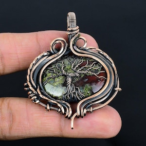 May include: A copper wire wrapped pendant featuring a green and red moss agate stone with a tree of life design. The pendant is oval shaped and has a copper bail.