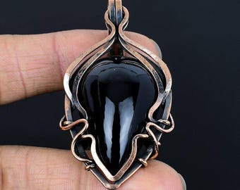 May include: A teardrop-shaped black onyx pendant with a copper-colored wire wrap. The pendant has a polished, reflective surface and is suspended from a copper bail. The wirework creates an ornate, open design around the stone.