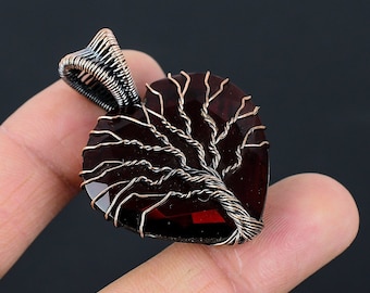 May include: A heart-shaped pendant with a copper wire tree design, set against a dark red gemstone.