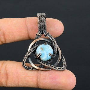 May include: A copper wire wrapped pendant with a blue and white gemstone in the center. The pendant is in the shape of a triangle with a circle around the gemstone.