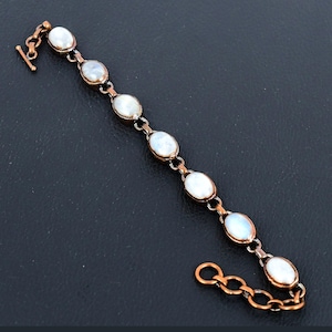 May include: A copper bracelet with oval-shaped white moonstone beads. The bracelet has a lobster clasp closure.