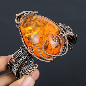 Op de afbeelding: Een armband van koperdraad met een grote amber edelsteen. De amber is druppelvormig en heeft een warme oranje kleur.