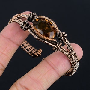 Op de afbeelding: Een armband van koperdraad met een bruine edelsteen in het midden.