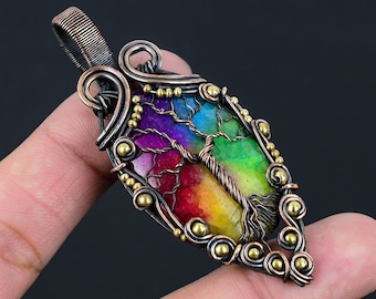 May include: A rainbow agate tree of life pendant with copper wire wrapping and gold beads. The pendant is on a finger.