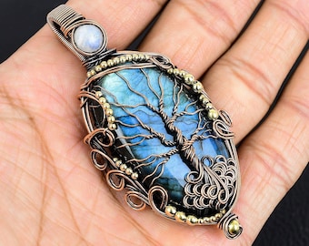 Könnte beinhalten: Ein drahtgewickelter Anhänger mit einem blauen Labradorit-Edelstein mit einem Baumdesign. Der Anhänger ist mit goldfarbenen Perlen und einem kleineren weißen Edelstein verziert.