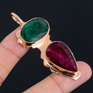 May include: A pendant featuring a green emerald gemstone and a red ruby gemstone set in gold.