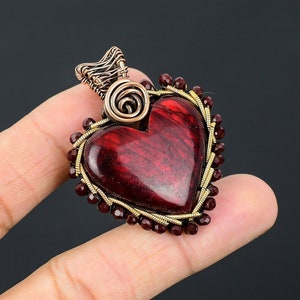May include: A red heart-shaped pendant with a wire-wrapped design and burgundy beads. The pendant is made of copper wire and has a gold finish.