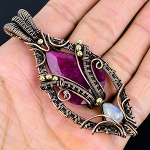 May include: A handcrafted pendant featuring a vibrant purple gemstone set in an intricate copper wire design. The pendant also includes a smaller, iridescent gemstone.
