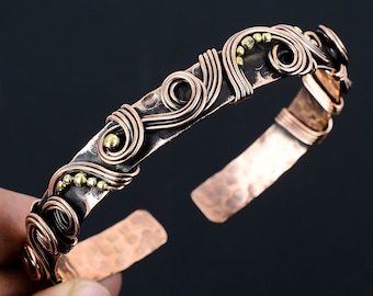 May include: A copper bracelet with a hammered finish and a decorative wire design featuring swirls and gold beads.