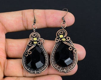 May include: A pair of black gemstone earrings with copper wire wrapping and gold accents. The earrings are teardrop shaped and dangle from a hook.